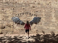 a woman walking in front of a brick wall with wings