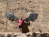 a woman standing in front of a brick wall with wings